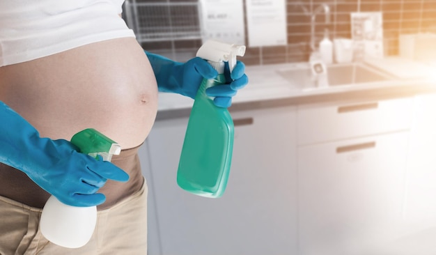 Foto sezione centrale di una donna incinta che tiene bottiglie di spray a casa