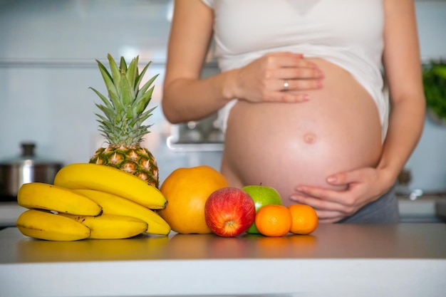 Midsection of pregnant woman holding stomach standing by fruit in kitchen at home