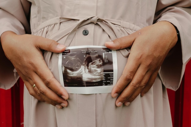 midsection of pregnant woman holding ultrasound photo by belly