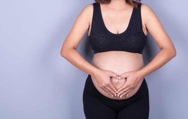 Midsection of pregnant woman making heart shape over abdomen over purple background