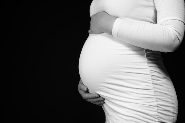 Foto sezione centrale di una donna incinta che tocca l'addome e si trova su uno sfondo nero