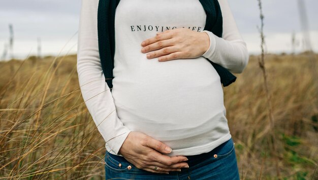 Midsection of pregnant woman touching abdomen while standing on grass
