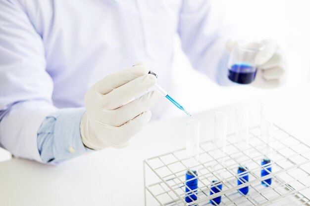 Photo midsection of scientist holding blue liquid in container at laboratory