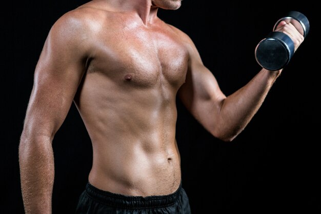 Midsection of shirtless athlete working out with dumbbell