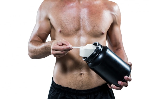 Midsection of shirtless man scooping up protein powder