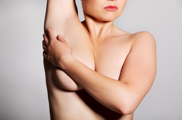 Foto sezione centrale di una donna senza camicia che copre il petto contro uno sfondo grigio