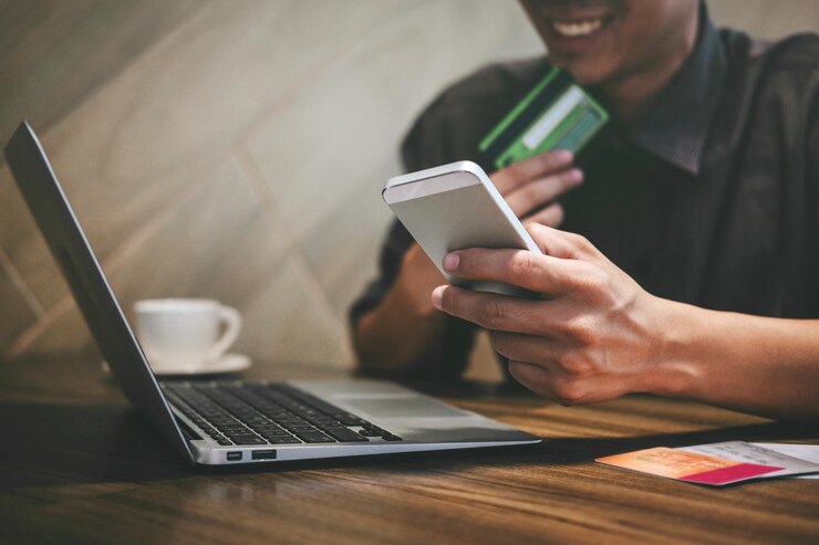 Photo midsection of smiling man using mobile phone while holding card by laptop on desk