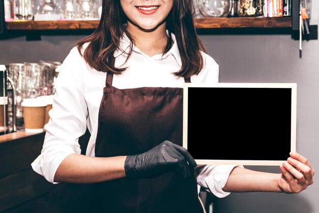 Foto sezione centrale di una donna sorridente con una lavagna vuota in piedi in un caffè