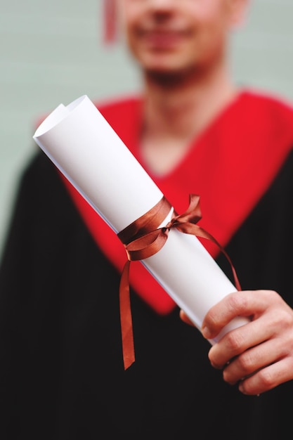 Foto sezione centrale di uno studente che indossa un abito da laurea mentre tiene in mano un diploma arrotolato