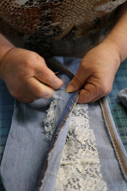 Photo midsection of tailor sewing lace on jeans