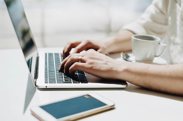 Midsection van een man die een laptop gebruikt met een mobiele telefoon en een koffiekop op tafel