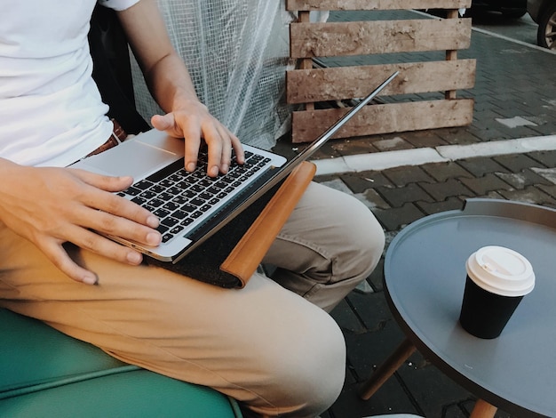 Foto midsection van een man die een laptop gebruikt terwijl hij koffie drinkt in een openluchtcafé