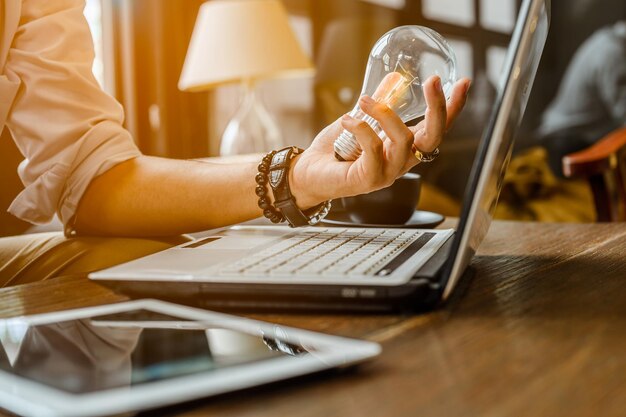 Foto midsection van zakenman die een gloeilamp vasthoudt terwijl hij aan een laptop werkt