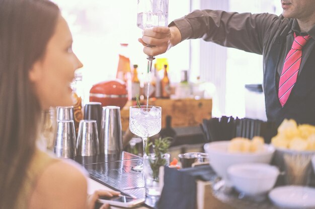 Midsection of waiter pouring drink in glass while woman standing by table