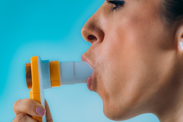 Midsection of woman blowing while holding asthma inhaler