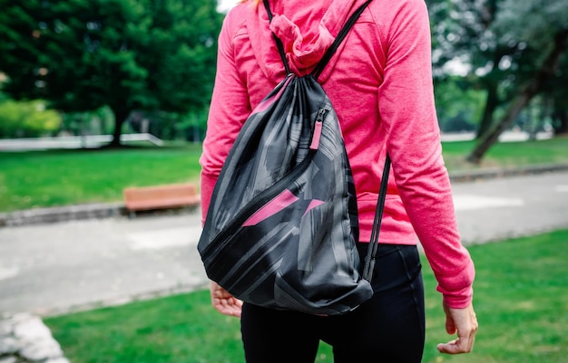 Midsection of woman carrying backpack while standing at park