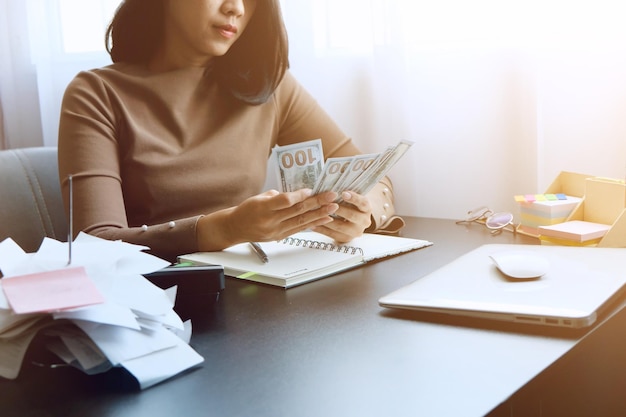 midsection of woman counting banknotes while sitting by table in office