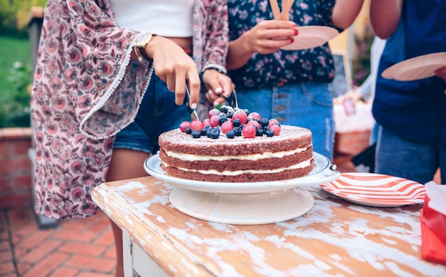 Photo midsection of woman cutting cake by friends at backyard