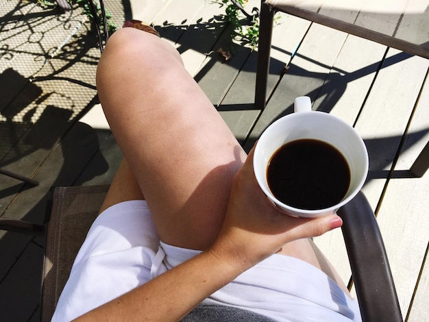 Photo midsection of woman holding black coffee cup while sitting with legs crossed at knee