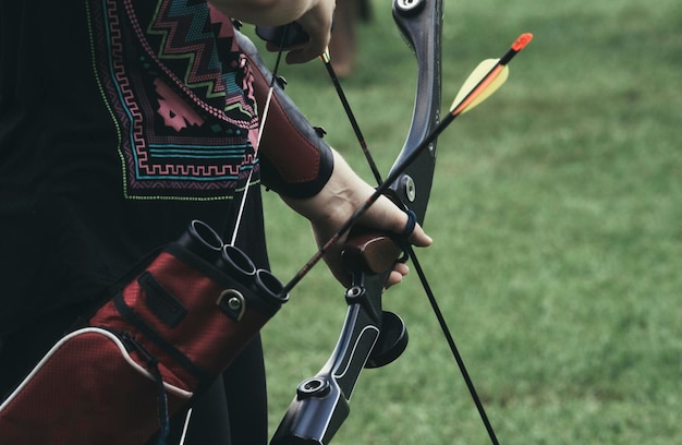 Midsection of woman holding bow and arrow on field