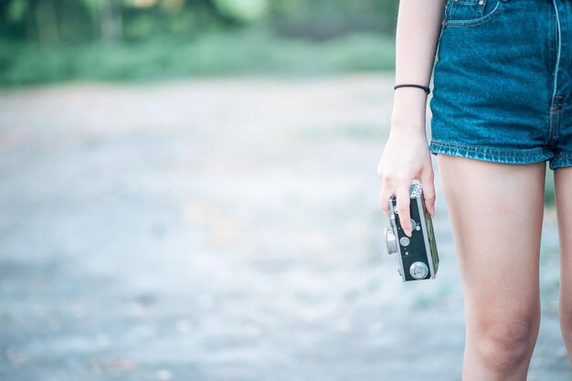 Midsection of woman holding camera while standing on land