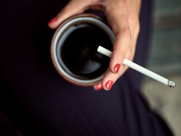 Foto sezione centrale di una donna che tiene una sigaretta e una tazza di caffè