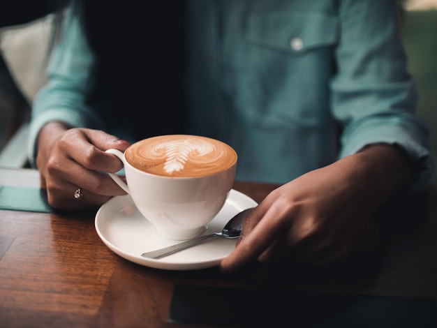 カフェのテーブルにコーヒーカップを握っている女性のミッドセクション