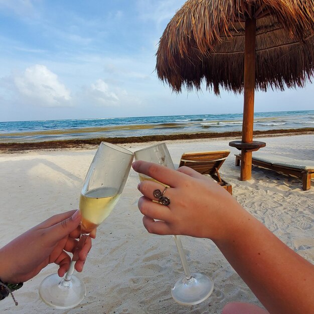 Midsection of woman holding drink at beach against sky