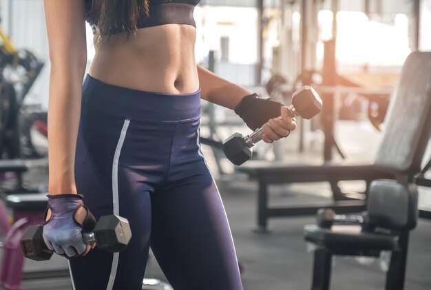 Midsection of woman holding dumbbells in gym