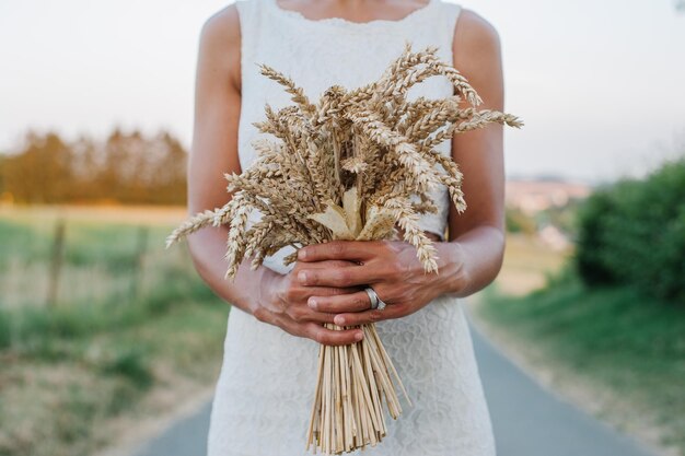 Foto sezione centrale di una donna che tiene un orecchio di grano mentre è in piedi sul campo contro il cielo