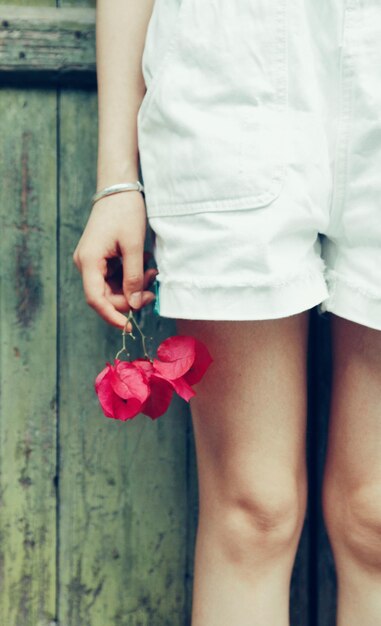 Foto sezione centrale di una donna che tiene un fiore mentre è in piedi contro il legno