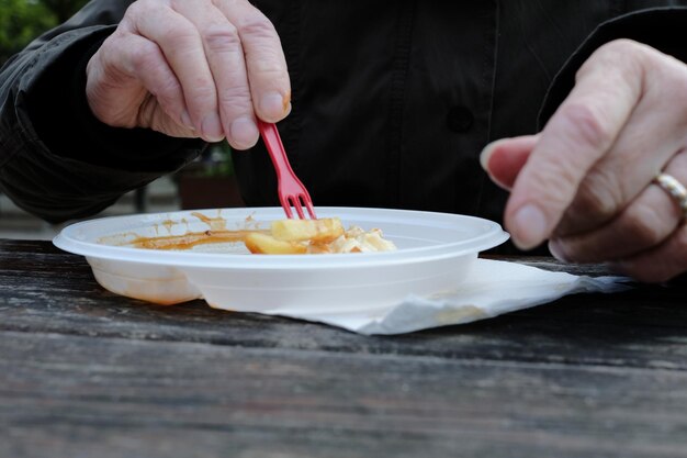 Midsection of woman holding fries in bowl on table