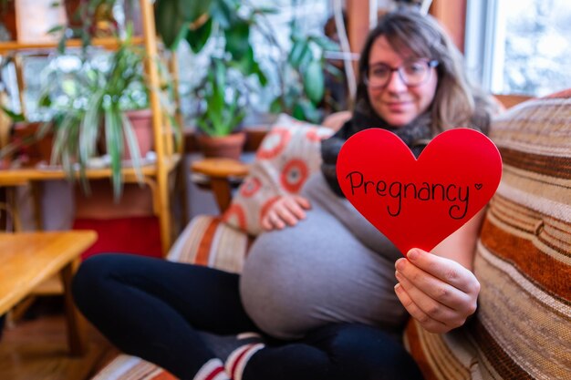 Foto sezione centrale di una donna che tiene la forma di un cuore mentre è seduta sul tavolo