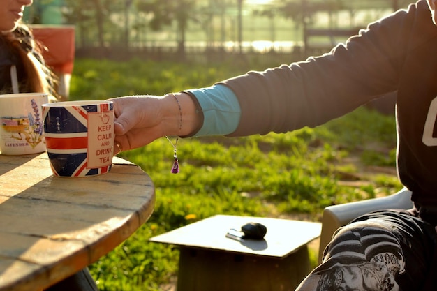 Photo midsection of woman holding mug while sitting in yard