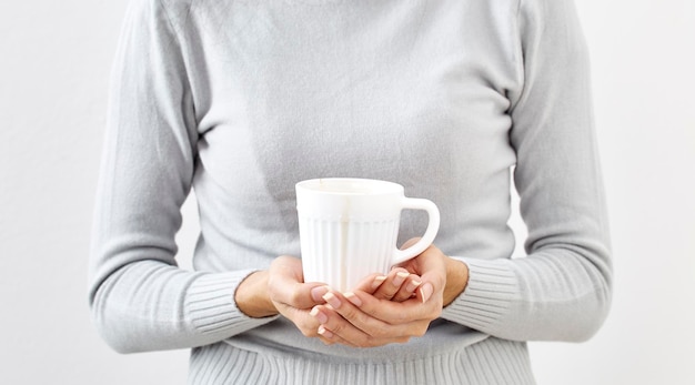 midsection of woman holding mug while standing against white background