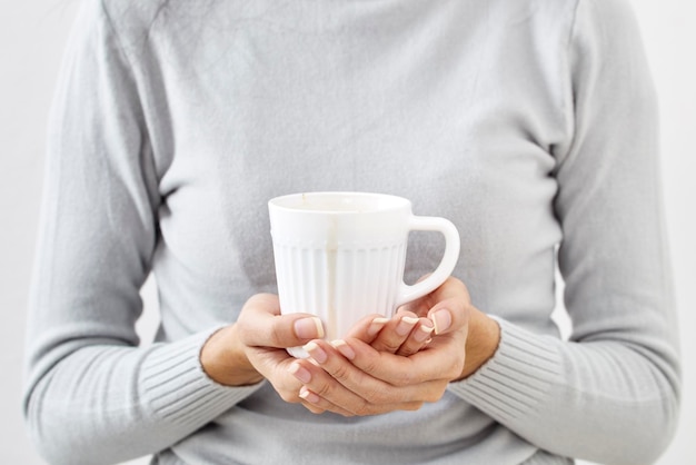 midsection of woman holding mug while standing against white background