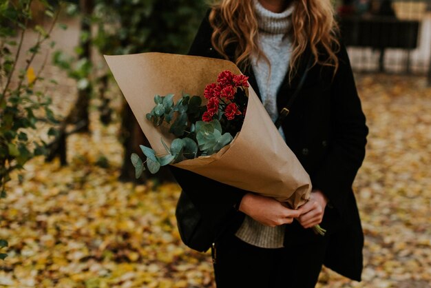 Photo midsection of woman holding wrapped bouquet in park during autumn