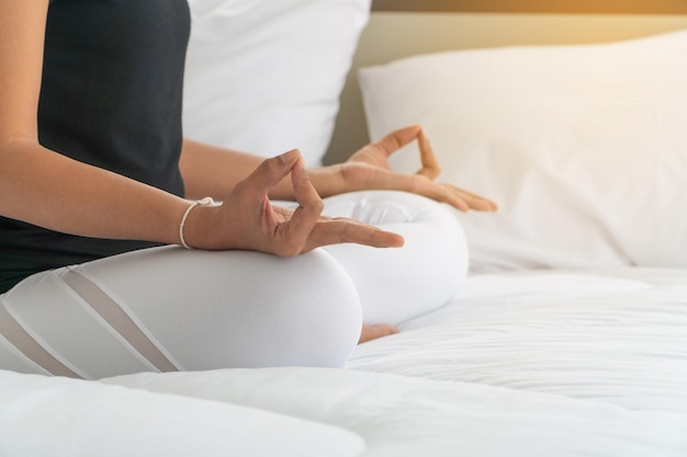 Midsection of woman meditating on bed at home