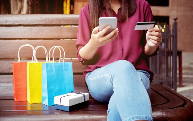 Photo midsection of woman online shopping using phone while sitting on bench