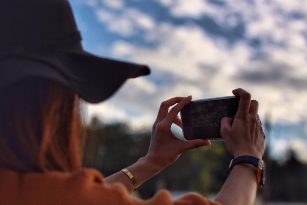 midsection of woman photographing with mobile phone against sky