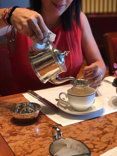 Photo midsection of woman pouring tea at table