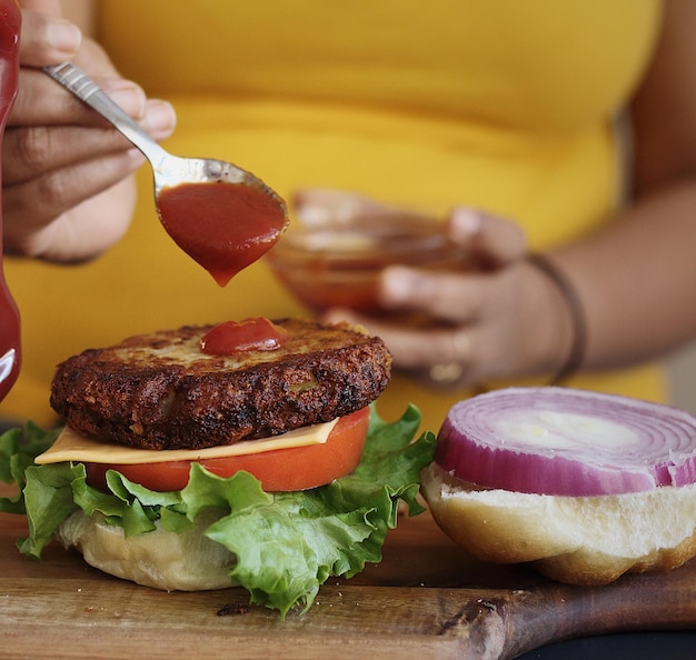 Foto sezione centrale di una donna che prepara un hamburger su un tavolo da taglio