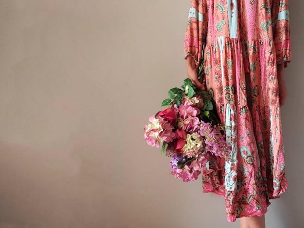 Photo midsection of woman standing against wall holding bouquet of flowers