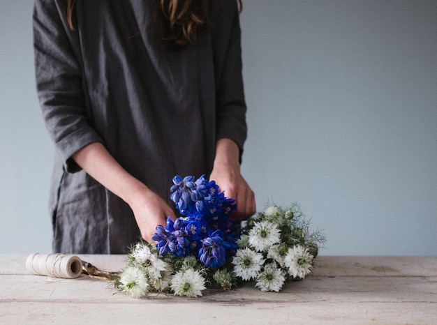 Photo midsection of woman tying flowers at table against wall