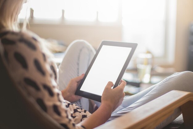 Photo midsection of woman using digital table while sitting on chair at home