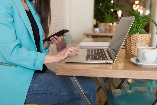 Midsection of woman using mobile phone by laptop at table