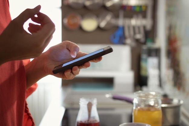midsection of woman using mobile phone in kitchen