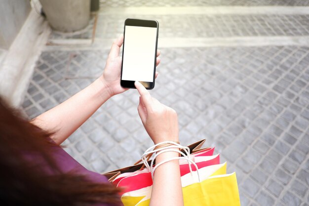 Foto sezione centrale di una donna che usa il telefono cellulare mentre tiene delle borse della spesa sul marciapiede