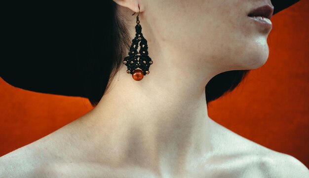 Midsection of woman wearing earring standing against red wall