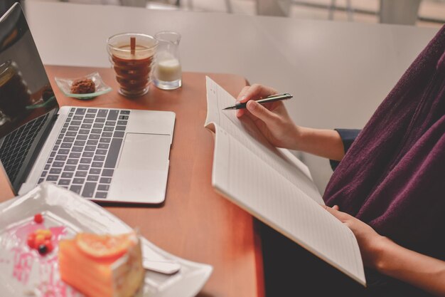 Photo midsection of woman wiring on book while working at desk in office